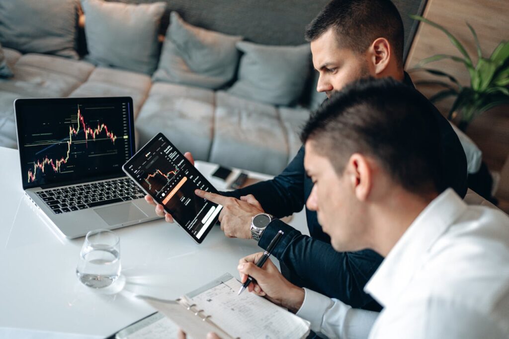 Two professionals analyzing stock market data on a tablet and laptop