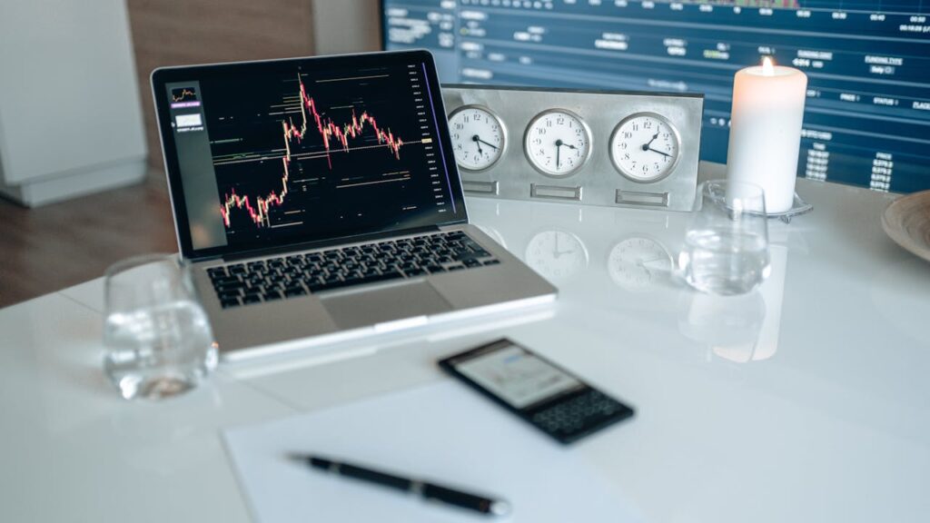 Investing for Beginners: Laptop displaying stock market chart on a desk with clocks and candle