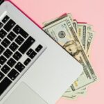 Investing online with a laptop and cash on a pink background