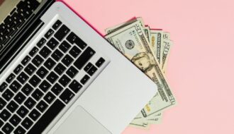 Investing online with a laptop and cash on a pink background