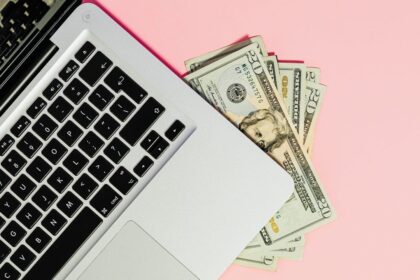 Investing online with a laptop and cash on a pink background