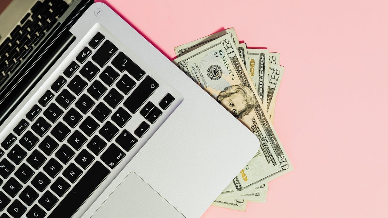 Investing online with a laptop and cash on a pink background