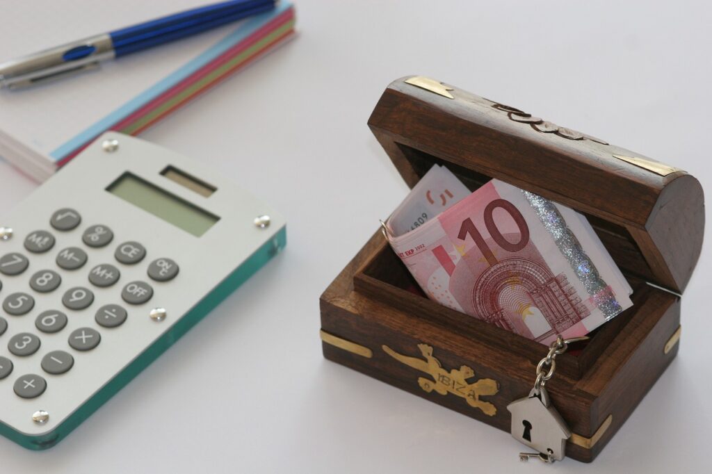 Calculator and notebook next to a wooden box with euro banknotes, symbolizing financial planning and savings